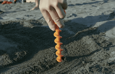 Orange screw tent stake inserting in sand